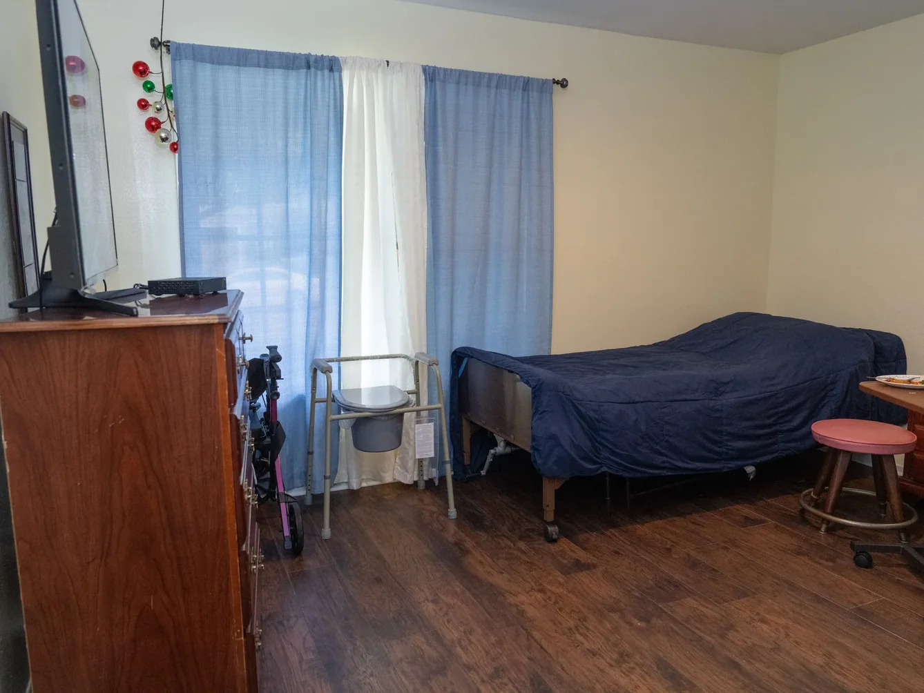 Spacious resident bedroom featuring hospital bed, bedside commode walker, and adaptive equipment in a comfortable home-like setting