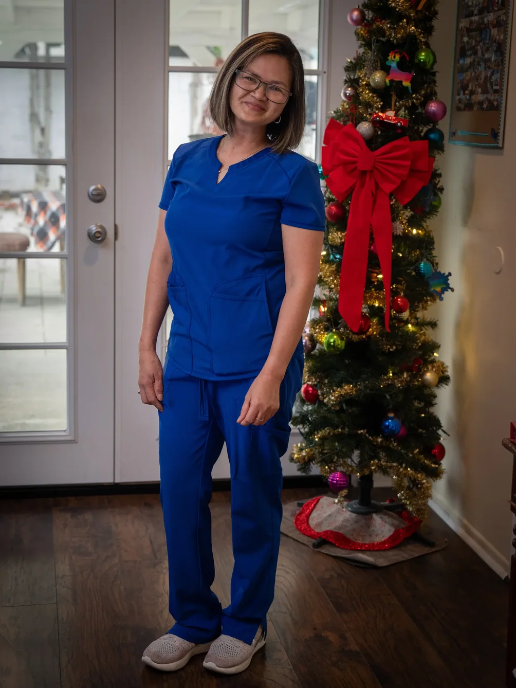 Caregiver in blue medical scrubs smiling in home setting with Christmas decorations